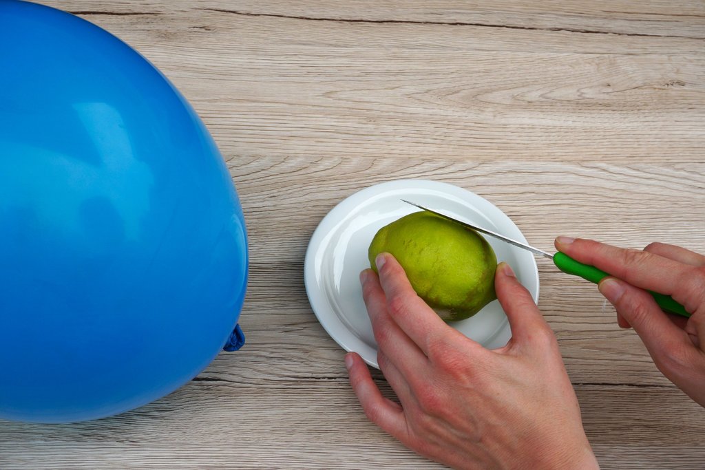 Blauer Ballon, Zitrone auf Teller, Hand mit Küchenmesser